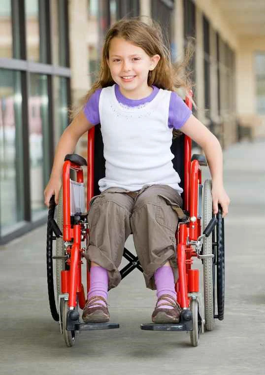 Lachend jongetje met krullen en sproeten in rolstoel 