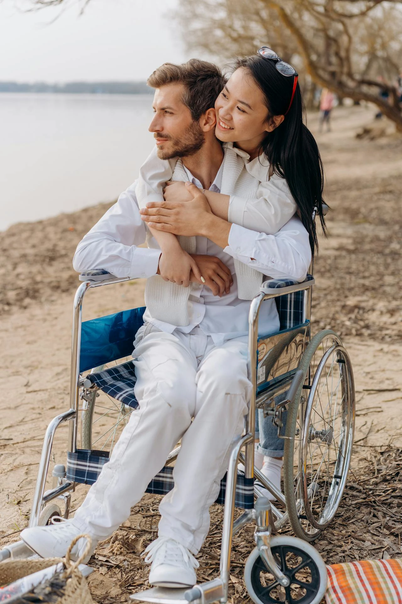Man in rolstoel omhelsd door vrouw op strand